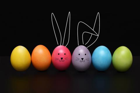A row of brightlyl-colored Easter eggs. Two have bunny ears and faces drawn on them.