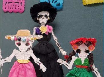 Three paper skeletons with crepe paper clothing and decorations