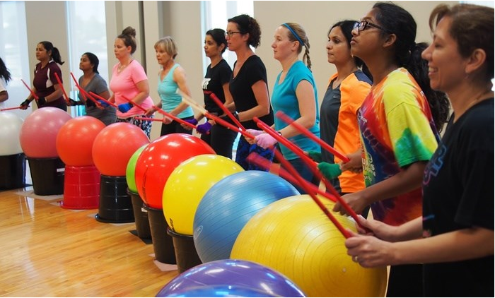 Row of women tapping sticks on large exercise balls