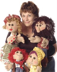A smiling woman surrounded by her puppet friends.