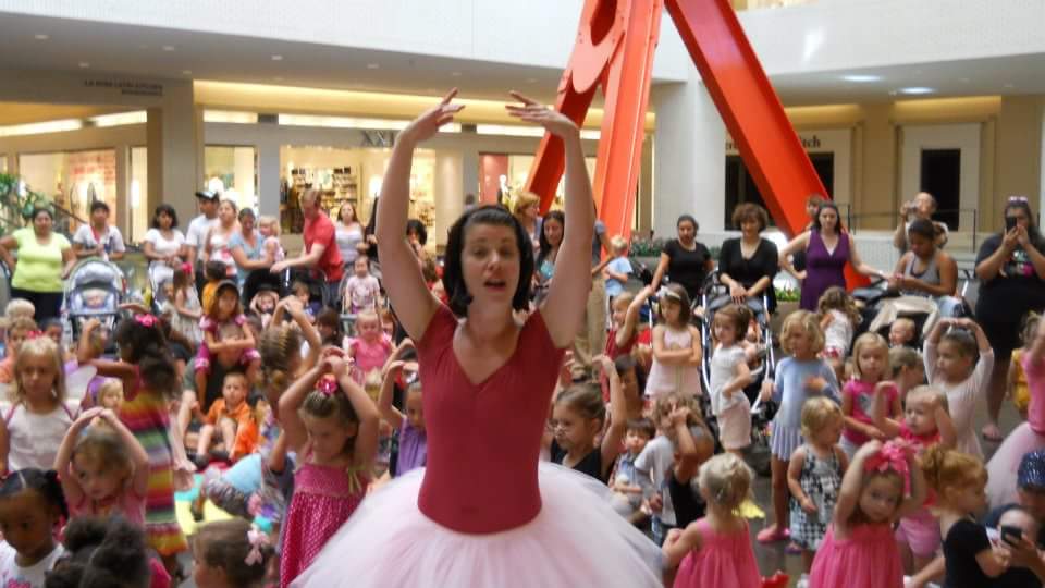 A ballerina dancing in front  of a group of young children.