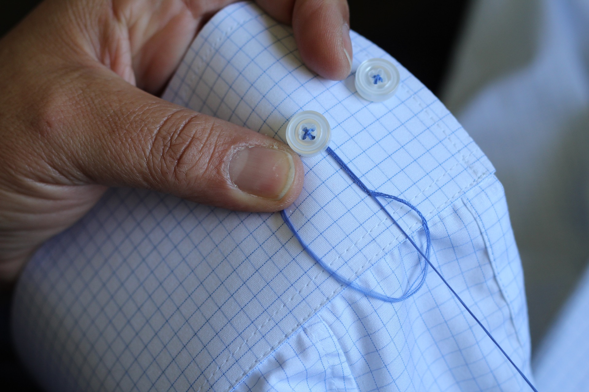 a hand sewing a white button onto the sleeve of a blue shirt