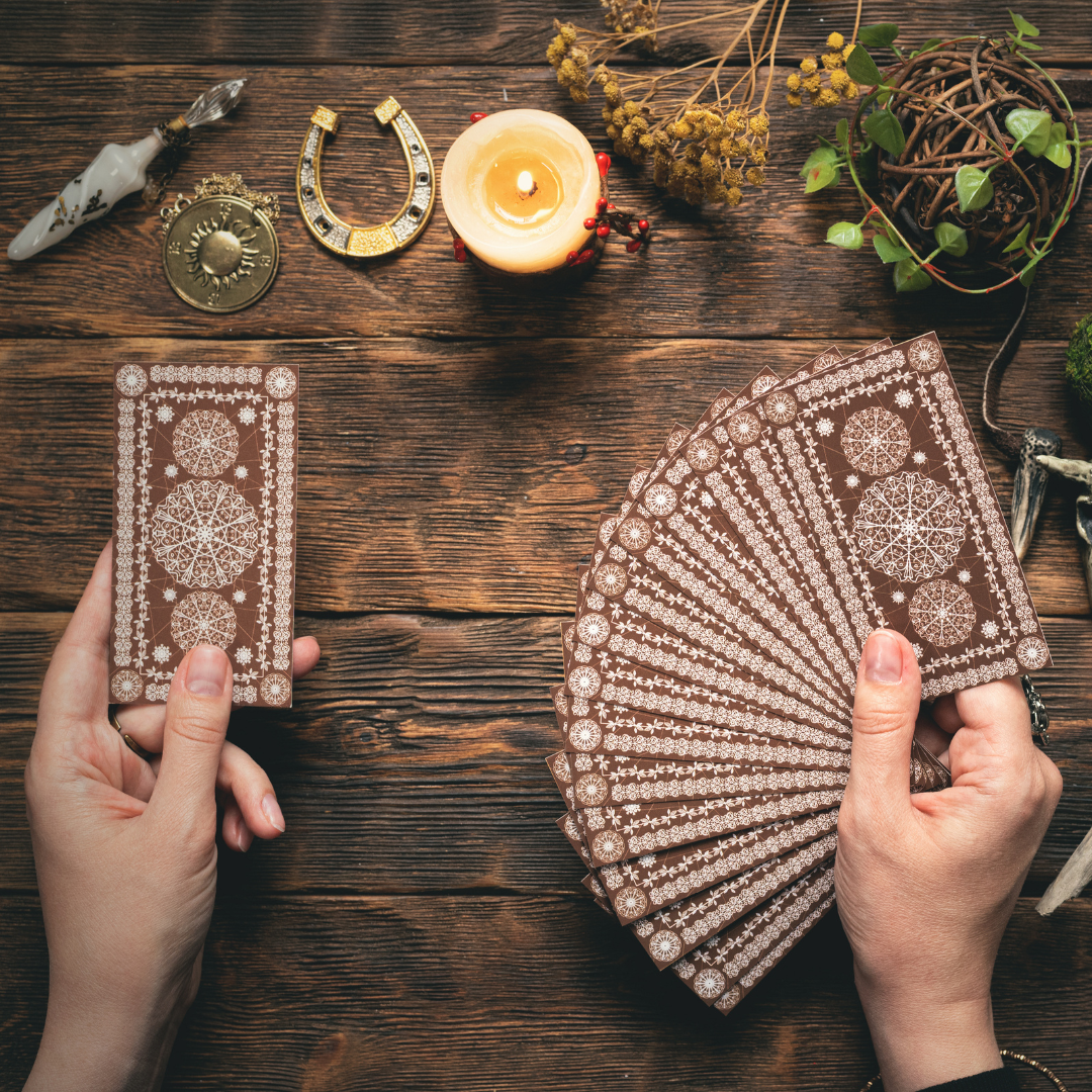 Hands holding a deck of tarot cards over a table.