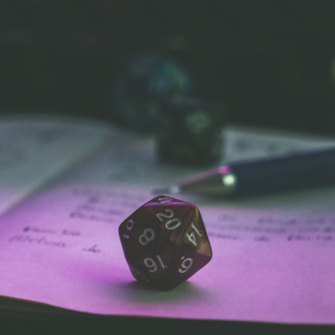 A 20 sided die resting on a notepad with a pen.