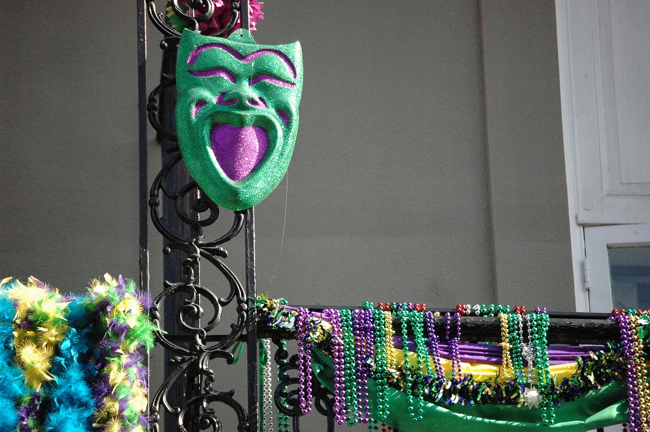 A wrought-iron balcony in New Orleans. It's decorated with blue and purple-gold-green feather boas, a green and purple comedy mask, many, many strings of beads and purple-gold-green bunting.