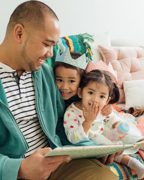 A sitting father reads a picture book to two children