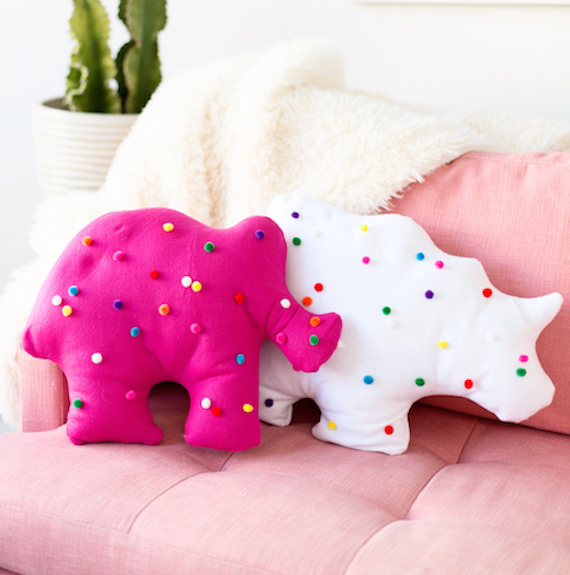 Pink and white pillows in the shape of animal crackers on a pink couch.