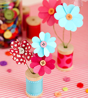 Colorful paper flowers displayed in a small, wooden spool "vase."