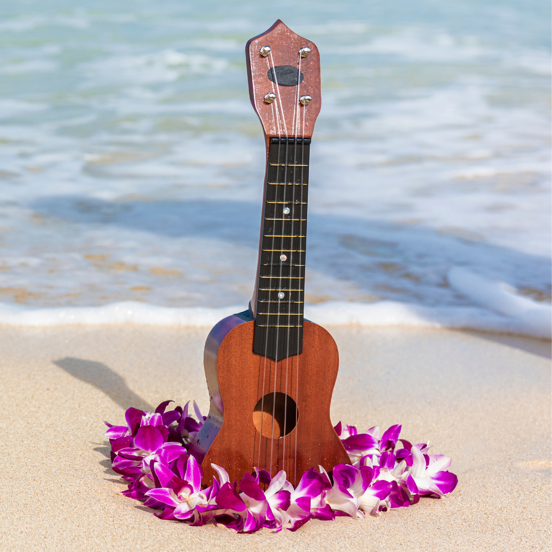 A ukulele and a lei sitting on the sand of a beach.
