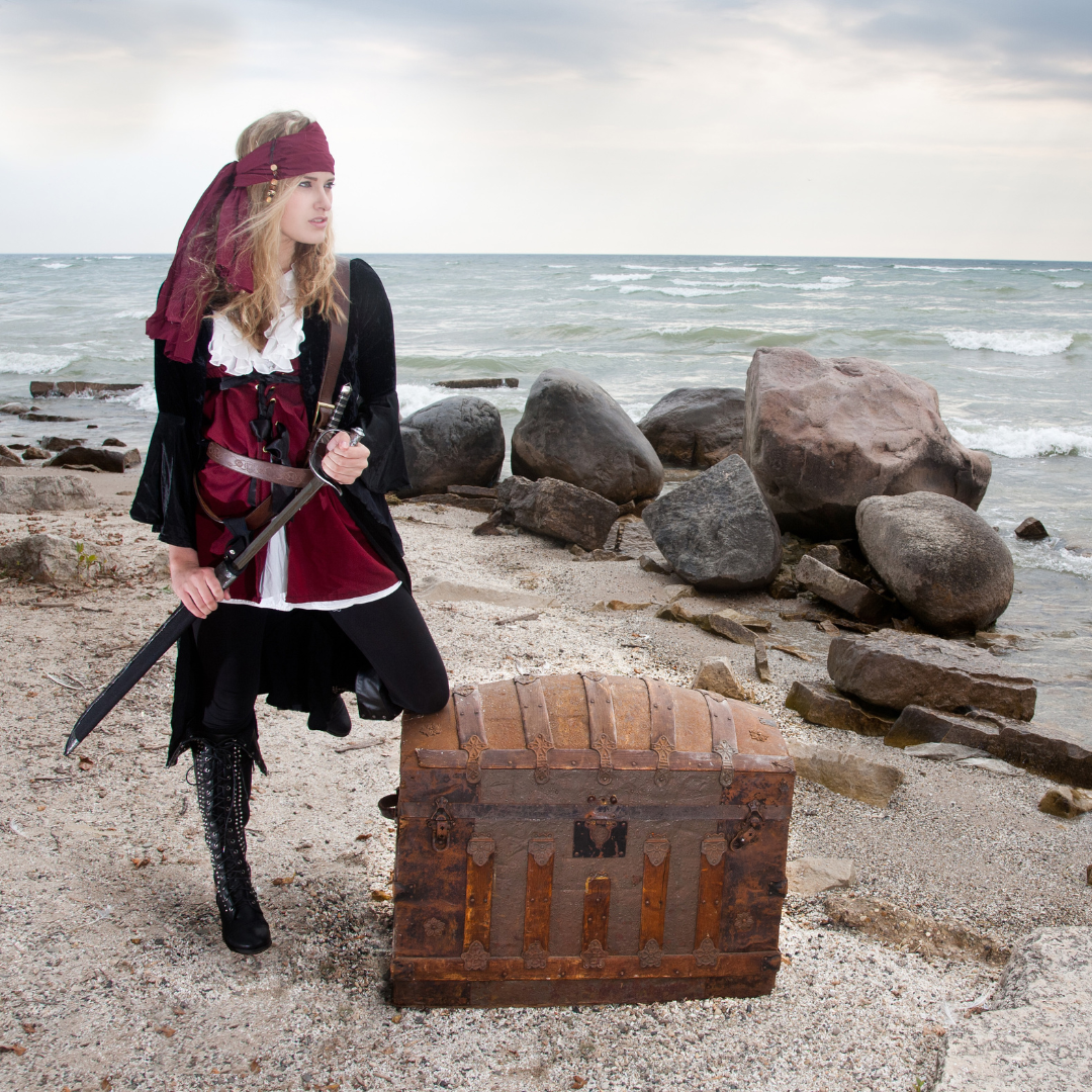 A stereotypical pirate with a treasure chest on a beach.