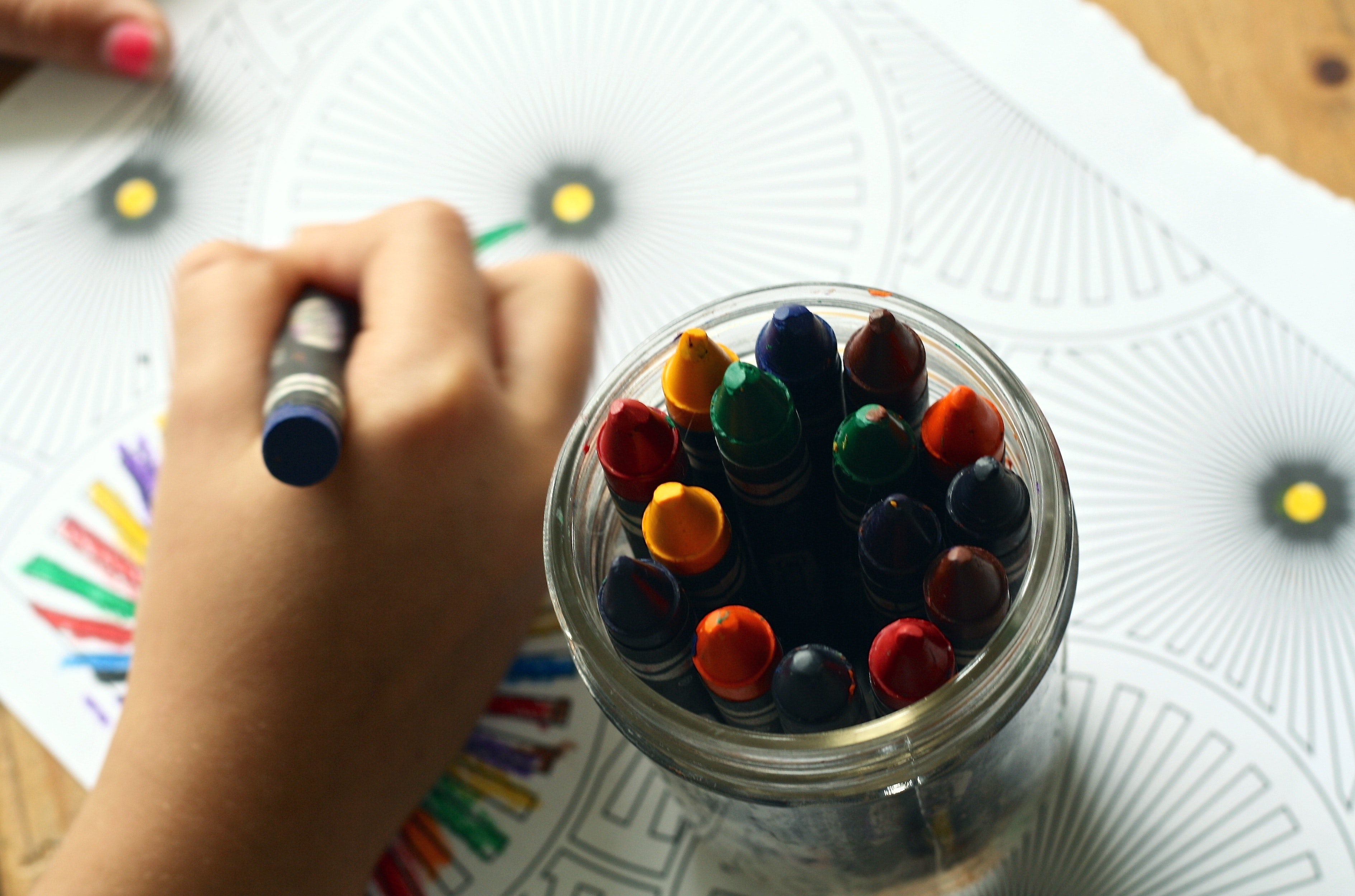 A child's hand colors a simple mandala coloring sheet with a crayon.