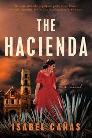 The cover of The Hacienda by Isabel Canas: A woman in a red dress stands among desert plants, a large, brick structure in the background.