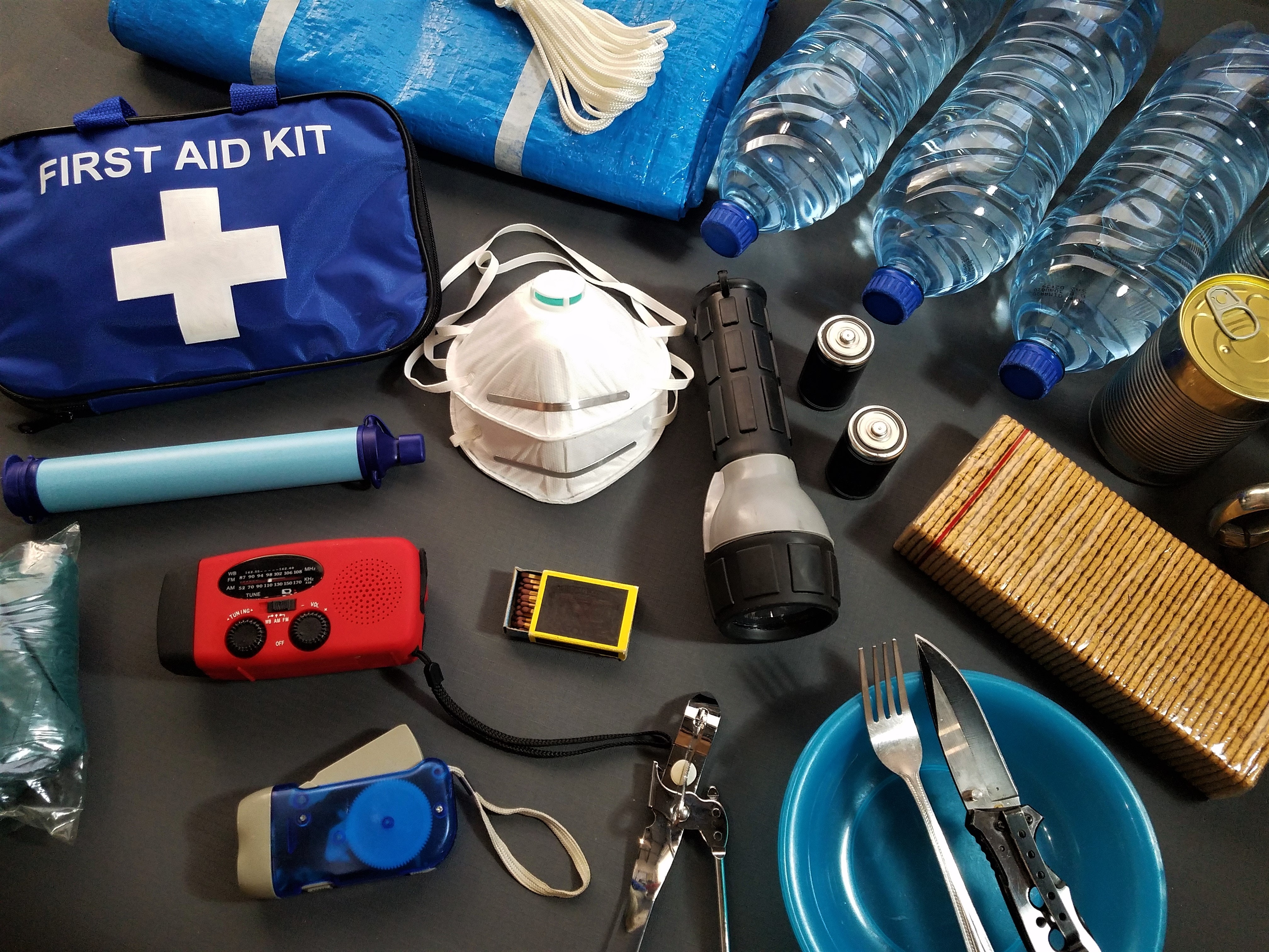 The contents of a typical emergency kit laid out on a table, including flashlight, masks, and first aid kit.