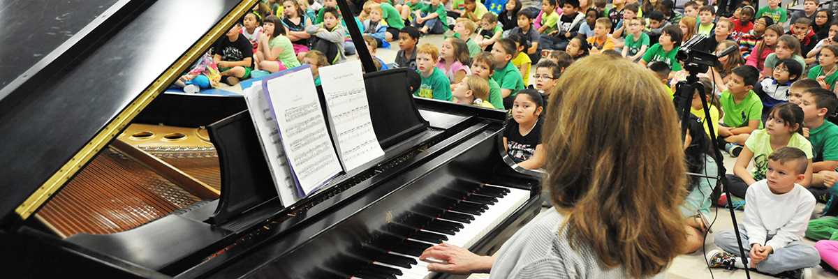 A pianist plays a piano for an audience of children.