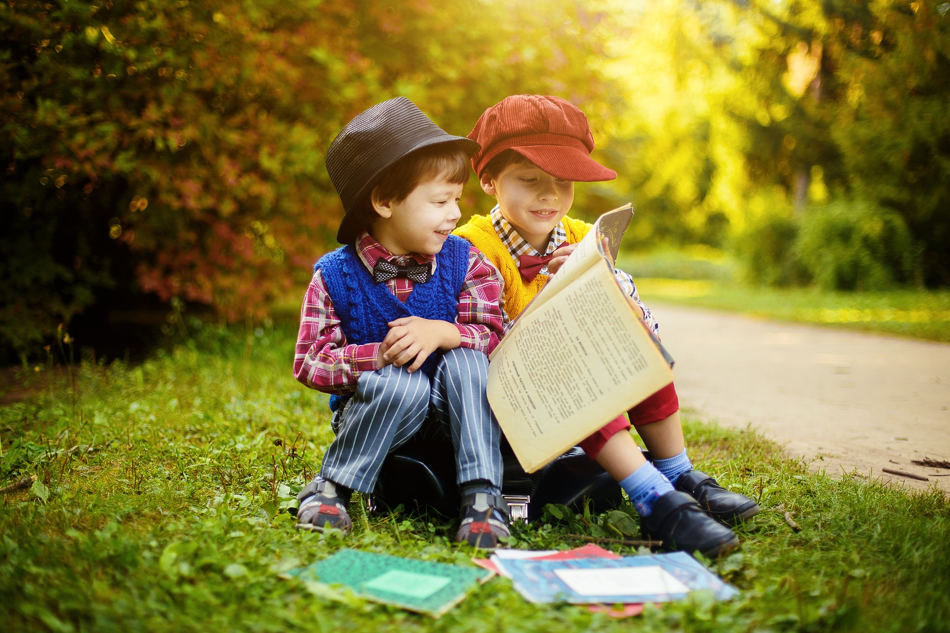 Two young boys sitting outside in early autumn looking at and reading a book