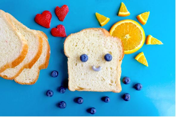 Bread and fruit arranged so a slice of bread has a smiley face