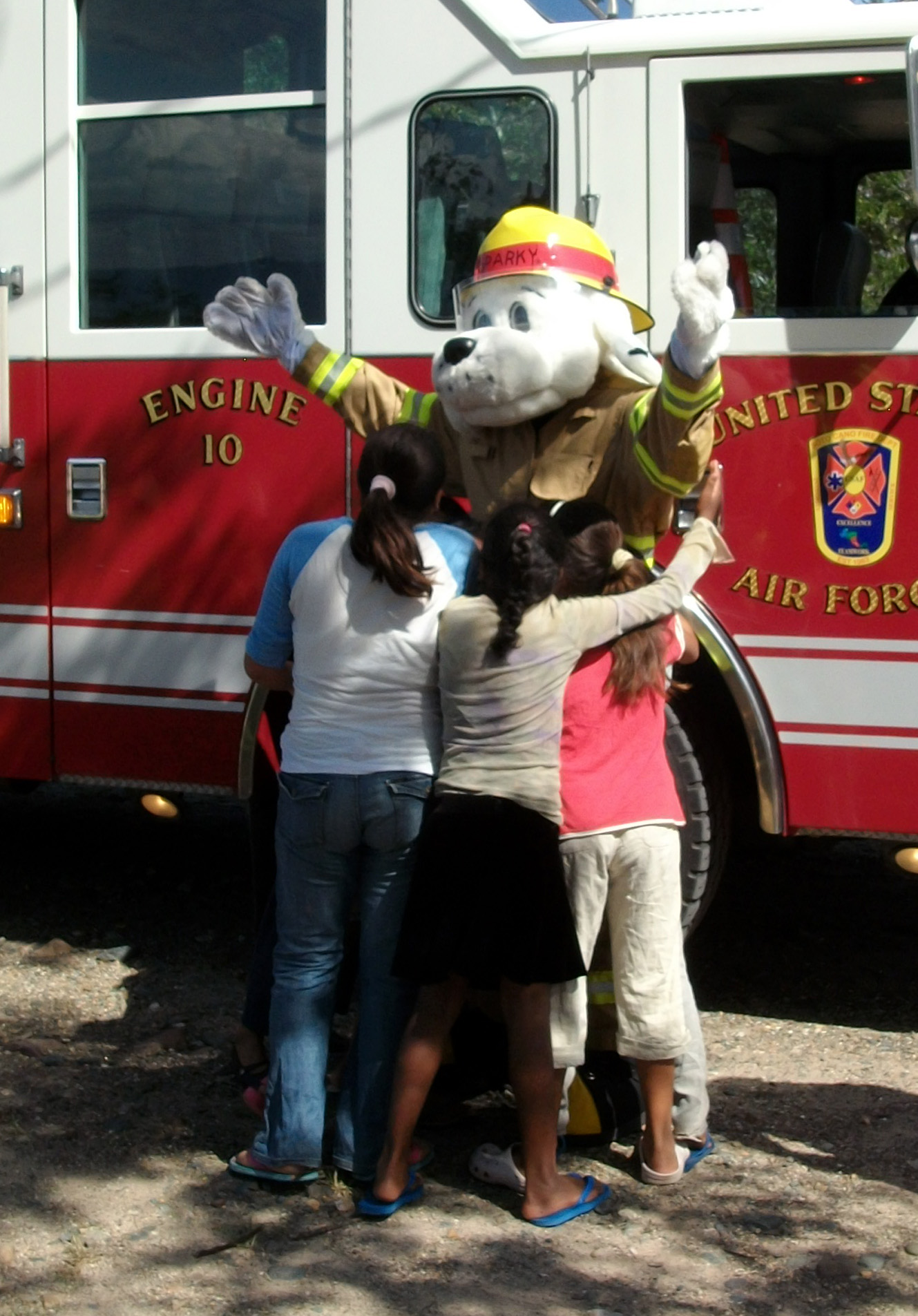 Sparky being hugged by children in front of a fire engine