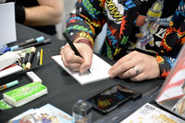 Artist with comic-themed sweatshirt working on a drawing