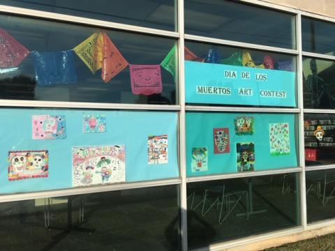 Photo of 10 student artworks on blue backing, surrounded by Dia de los Muertos decorations