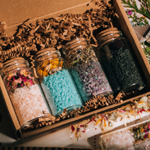 Differently colored bath salts with dried botanicals in corked jars.