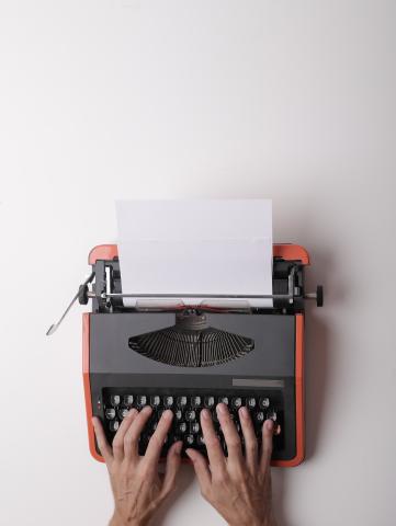 A pair of hands hover over the keys of a red typewriter.