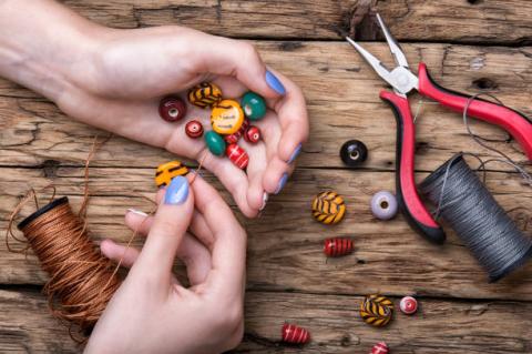 Hands Putting Beads on a String with Pliers Sitting in the Background