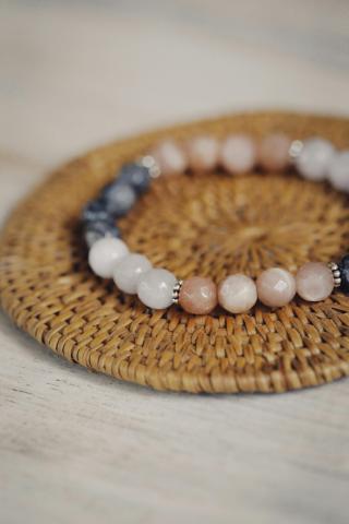 A beaded wire bracelet sitting on a whicker coaster. The spherical beads are various shades of brown, white, and black and have small silver rings separating the colors.