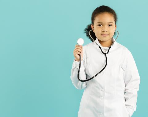 A young girl looking serious in a white doctor’s coat holding up a stethoscope at shoulder level. She is on a cyan background.