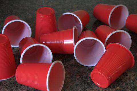 12 red solo cups randomly spread out on a floor. 10 are on their sides. 2 are upside down.