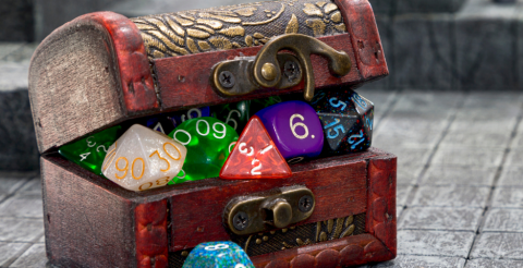 A red and gold treasure chest sits on a gray tiled surface. The chest is crammed full of multi-colored polyhedral dice, so many that the lid can't close.