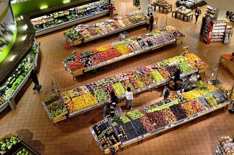 An overhead view of the produce section of a grocery store. There are 4 aisles of produce in the middle of the area, leafy greens line the left side. The bakery section possibly begins on the right side of the image.