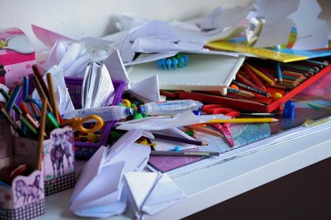 A white desk covered in clutter. There are pencils, scissors, folded pieces of paper, and pencil cups with horses on them.