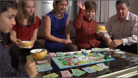 five family members sit around a coffee table playing a game of monopoly