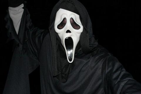 a person wearing a Ghostface costume looks into the camera