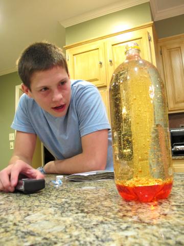 A boy looks on a red lava lamp he made in a 2 liter bottle.