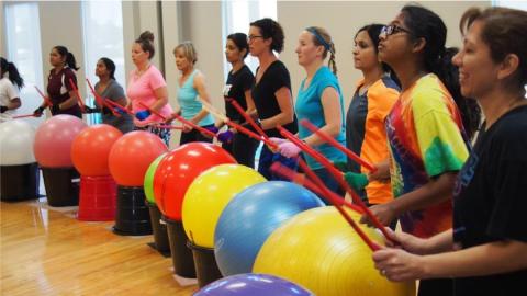 people using drum sticks, balls, and buckets to exercise