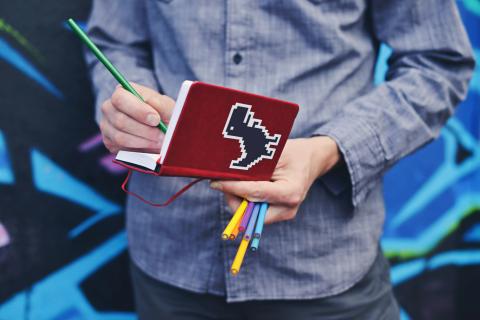 man writing in notebook with t-rex sticker on cover