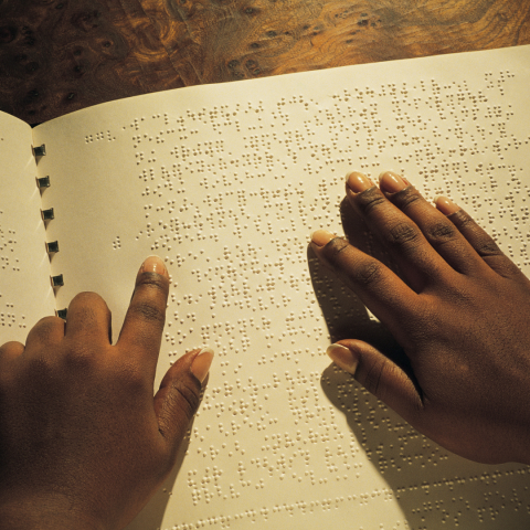 Black hands reading braille on a white page