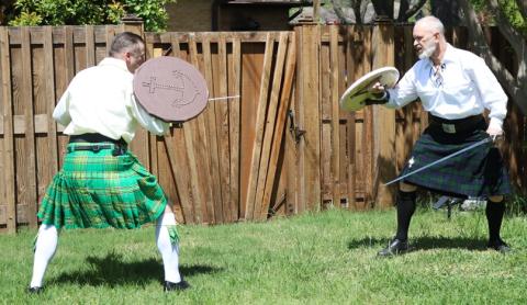 two males in kilts demonstrating sword techniques