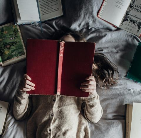 a young girl surrounded by books, reading while lying down