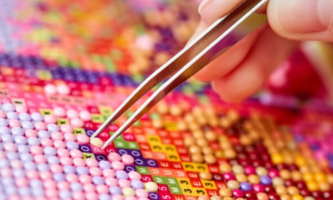 hand holding tweezers to place small squares onto a page
