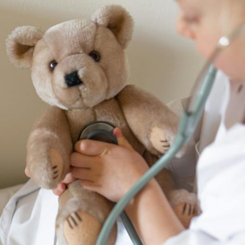 A child holds a stethoscope up to a teddy bear's chest.