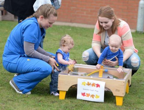 Two adults and two toddlers interact and play with a sensory bin.