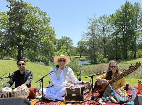 Three people sitting in a park playing Indian and Middle Eastern instruments