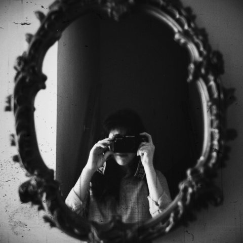 Black and white photo of person holding a camera and taking a photo of themselves in the mirror