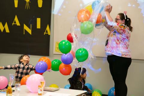 An adult pouring a bag full of balloons on an ecstatic child