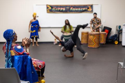 Dancers and drummers performing while a woman in blue watches and claps