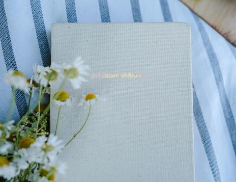 grey journal with text "book journal" next to white flower on a blue striped cloth