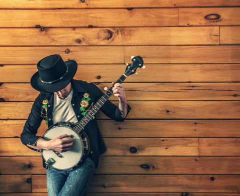 man in western wear playing banjo in front of a wood paneled wall