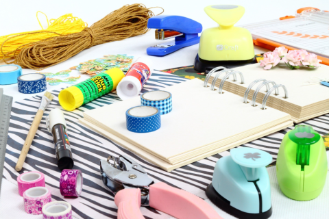 scrapbook supplies laid out on a table, hole punches, washi tapes, string, scissors, glue stick and a notebook